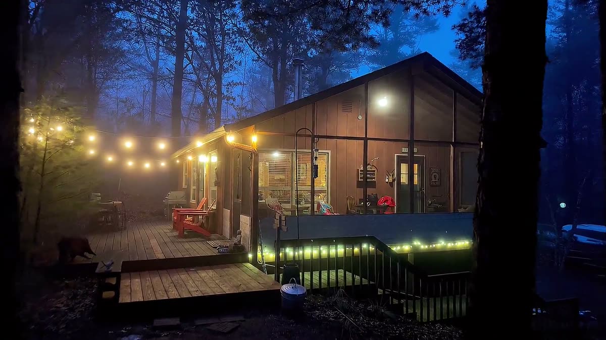 A cabin deck at dusk, string lights on, windows lit from inside